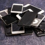 Celulares antigos e aparelhos eletrônicos empilhados sobre um fundo cinza.