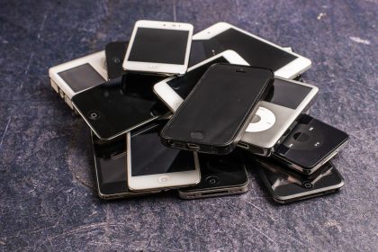 Celulares antigos e aparelhos eletrônicos empilhados sobre um fundo cinza.