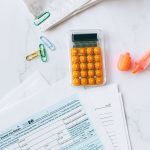 Formulários financeiros, calculadora e materiais de escritório organizados sobre uma mesa.