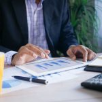 Homem analisa dados financeiros em um tablet em um ambiente de escritório.