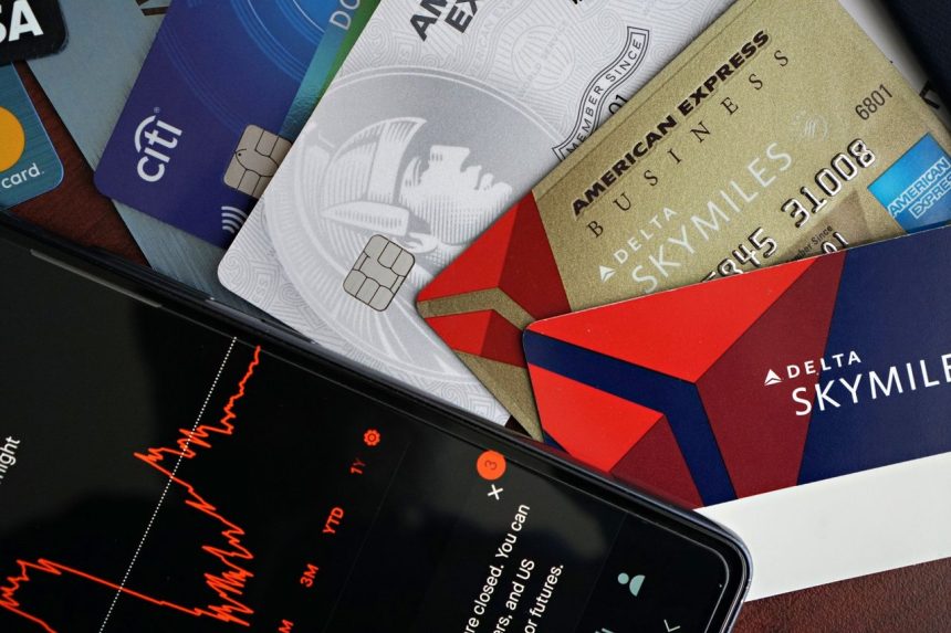 Cartões de crédito ao lado de um smartphone que exibe um gráfico do mercado financeiro.