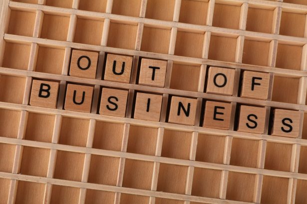 Blocos de madeira formam a expressão “Out of Business” sobre uma superfície de madeira, simbolizando o encerramento de uma atividade.