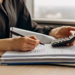 Pessoa usando uma calculadora sobre documentos financeiros em um escritório.