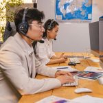 Agentes de atendimento trabalham diante de computadores usando fones de ouvido em um ambiente de call center.