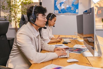 Agentes de atendimento trabalham diante de computadores usando fones de ouvido em um ambiente de call center.
