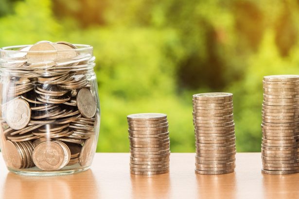 Mão segurando uma cédula de dólar sobre moedas e dinheiro, em uma composição conceitual sobre finanças, depósitos e investimentos.
